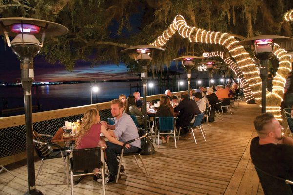 diners on the deck of caps on the water at night under lights
